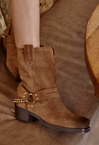 A close-up of a person's leg wearing a brown suede western-style boot with a dark brown block heel
